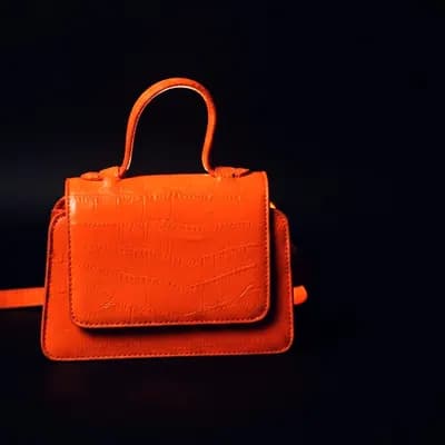An orange structured leather handbag lit against a black background