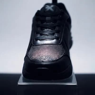 A black sneaker lit on a dark acrylic plinth like a museum piece